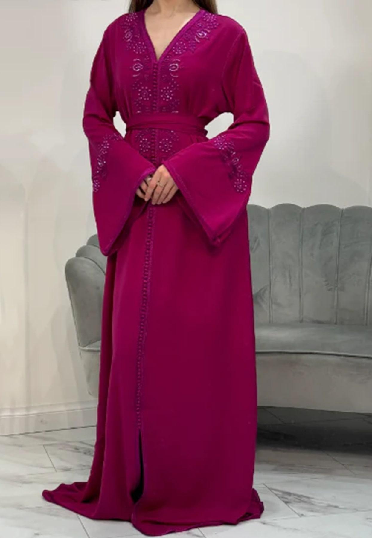 A woman wearing a pink full-length kaftan with embellishments on the neckline and sleeves