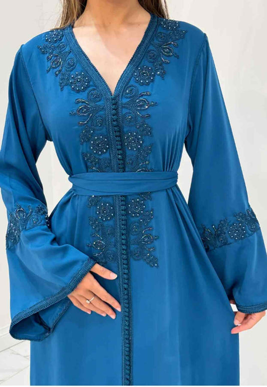 A woman wearing a blue kaftan with intricate detailing and a belt at the waist.